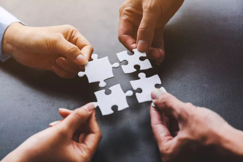 A close-up shot of four hands holding puzzle pieces that seamlessly fit together, illustrating successful teamwork, collaboration, and problem-solving